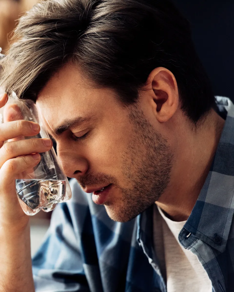 Man pressing a cold water bottle to his forehead