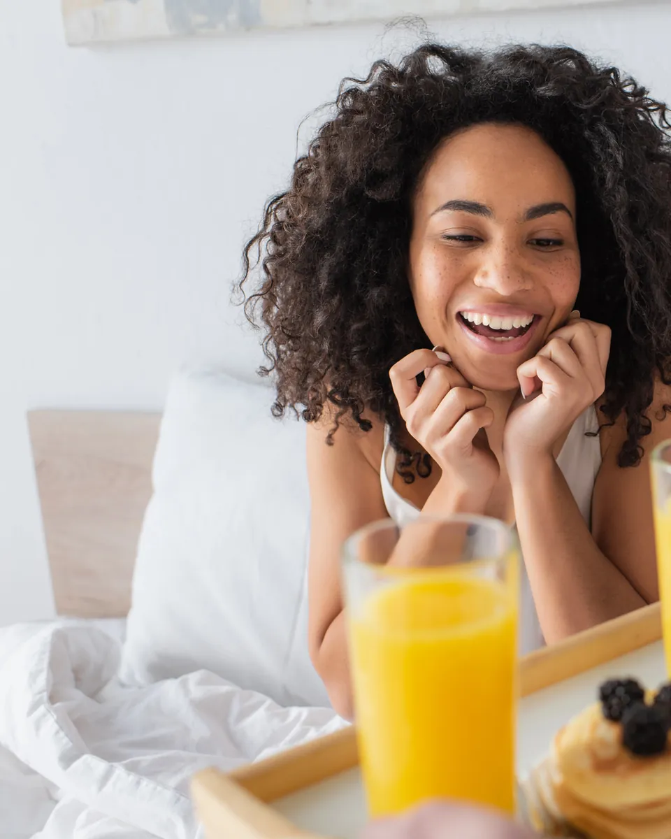 Woman smiling over breakfast in bed with orange juice